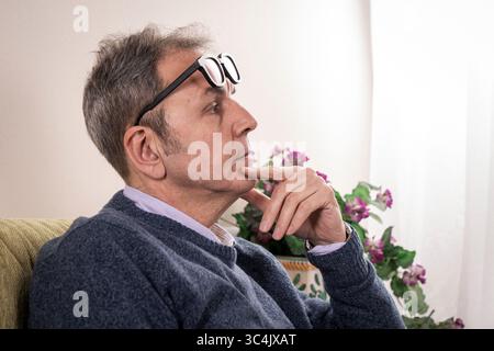 Primo piano introspettivo di un uomo di mezza età con la mano sul mento, con occhiali ribaltabili sulla fronte mentre contempla una prob Foto Stock