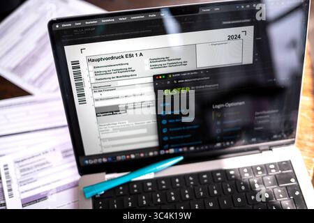 ILLUSTRAZIONE - 29 luglio 2025, Brema: Un computer portatile con il software della dichiarazione dei redditi ELSTER aperto mostra il modulo principale per la dichiarazione dei redditi 2024. I moduli fiscali stampati possono essere visualizzati in background. La scadenza regolare per la presentazione della dichiarazione dei redditi 2024 è il 31 luglio 2025 - si applica una scadenza prorogata per l'assistenza dei consulenti fiscali. Foto: Sina Schuldt/dpa Foto Stock