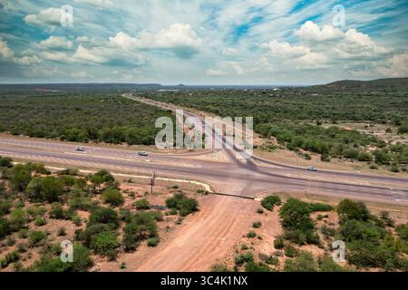 veduta aerea intersezione autostradale con carrozze stradali, autobus, camion, su paesaggio africano cespuglio e colline, nuovi sviluppi nei trasporti, giorno Foto Stock
