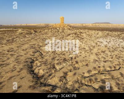 Vista aerea del paesaggio arido e soleggiato, dove una formazione rocciosa torreggiante sorge dalla terra asciutta, incisa con ombre e vegetazione arroccata, da Foto Stock