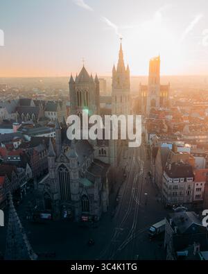 La vista aerea della guglia della chiesa di San Nicola si erge maestosamente sopra il paesaggio storico della città, bagnata dal caldo bagliore del sole che tramonta, Gent, Fiandre, Belgio. Foto Stock