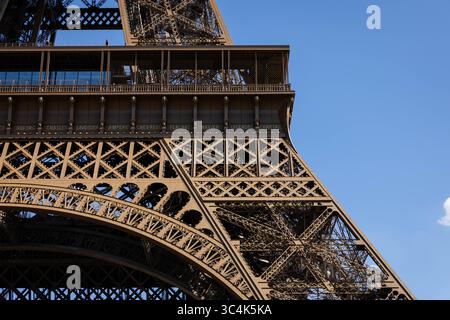 Primo piano dell'intricato reticolo della Torre Eiffel contro un cielo blu vibrante. L'immagine mostra i dettagli architettonici della torre e le decorazioni desi Foto Stock