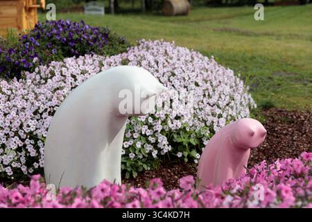 Affascinanti sculture in mezzo a fiori vivaci: Una tranquilla scena di creatività e bellezza della natura intrecciata con il cemento e la colorata Flora Foto Stock