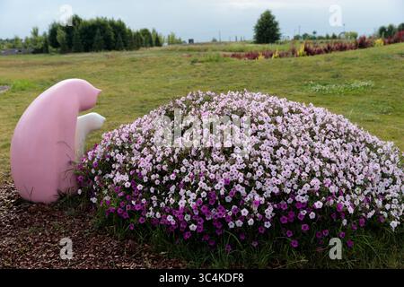 Stravagante scultura in giardino circondata da colorate Petunias: Un momento sereno catturato nella natura con i fiori rosa e viola che esaltano il divertimento Foto Stock