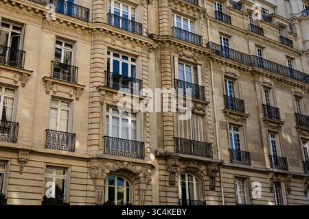 Elegante facciata parigina dell'edificio di appartamenti, con balconi e finestre ornati. La calda pietra beige contrasta con le ringhiere in metallo scuro. Ideale per Foto Stock