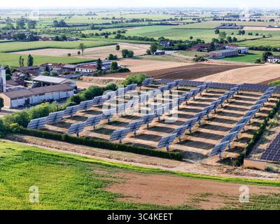 Veduta aerea di pannelli solari crogiolati al sole vicino al campo agricolo, in netto contrasto con il verde del paesaggio, Cavallermaggiore, Piemonte, Foto Stock