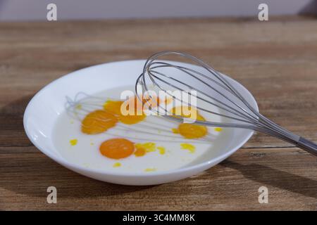 Una vista ravvicinata delle uova fresche mescolate con latte in una ciotola bianca su una superficie rustica in legno per deliziose creazioni culinarie e fatte in casa Foto Stock