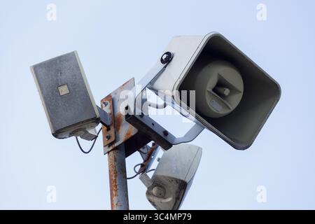 Un array multiforme di altoparlanti per esterni montati su un palo metallico contro un cielo blu chiaro, che mostra il design e la funzionalità di Public Address Foto Stock