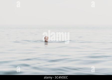 Man Water Ocean Drowning - Un solo uomo è in acqua, con solo la testa e un braccio visibili. Sta lottando per rimanere a galla e sembra esserlo Foto Stock