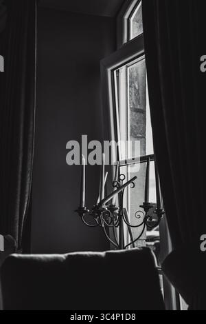 Foto di una finestra in una vecchia casa, vicino alla finestra c'è un grande candelabro con candele, due candele sono rotte. Foto Stock