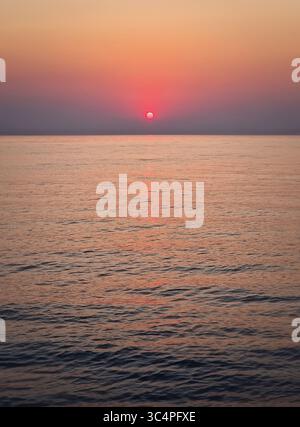 Accattivante alba sul mare calmo. Tranquillo paesaggio marino all'alba con morbide sfumature di arancione e rosa sul cielo che si riflettono sull'acqua Foto Stock