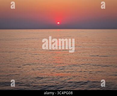 Accattivante alba sul mare calmo. Tranquillo paesaggio marino all'alba con morbide sfumature di arancione e rosa sul cielo che si riflettono sull'acqua Foto Stock