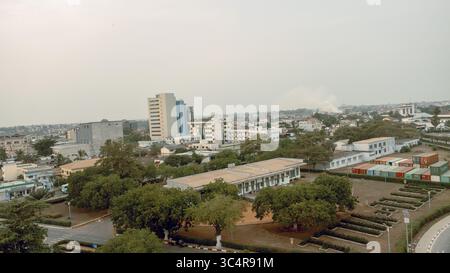 Vista aerea di un paesaggio urbano dove edifici moderni sorgono in mezzo a una vegetazione lussureggiante, con pile di contenitori che aggiungono un tocco di contrasto industriale, Lomé, regione marittima, Togo. Foto Stock