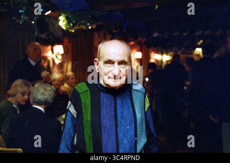 Ritratto uomo anziano, 00-01-1998 Whizgle News, Dutch Desk, Paesi Bassi, 1950-2000 un uomo anziano sorride calorosamente, vestito con un maglione colorato a righe, in mezzo a un vivace ritrovo in un ambiente accogliente pieno di luci soffuse e decorazioni festose. Foto Stock