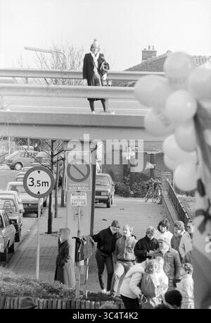 Sfilata di Carnevale, Noordwijkerhout, Carnival, Noordwijkerhout, 07-02-1986 Whizgle News, Dutch Desk, Paesi Bassi, 1950-2000 Una donna si trova su un cavalcavia mentre una folla si riunisce sotto, molte interagiscono e si godono il momento. Nelle vicinanze, mongolfiere e cartelli stradali aggiungono un tocco di vivacità all'atmosfera della scena. Foto Stock