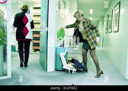 Miscellaneous, camera di commercio, Amsterdam, Amsterdam, Paesi Bassi, 07-03-1999 Whizgle News, Dutch Desk, Paesi Bassi, 1950-2000 due donne si trovano in un ufficio professionale. Una donna indossa un maglione a motivi geometrici e getta un oggetto verde in un cestino della spazzatura. L'altra donna, vestita con un cappotto elegante, si allontana sullo sfondo. Lo spazio è caratterizzato da armadietti per archiviazione e pareti di colore chiaro, creando una tipica atmosfera da ufficio. Foto Stock