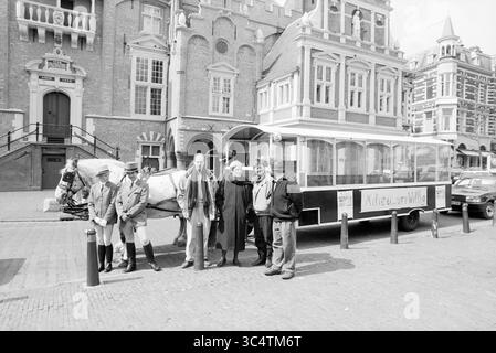 Tram a cavallo Haarlemse Vosse con poster: Ambiente volontario, di fronte al municipio di Haarlem, Haarlem, Grote Markt, Paesi Bassi, 00-04-1989 Whizgle News, Dutch Desk, Paesi Bassi, 1950-2000 Un gruppo di sei persone si trova di fronte a un grande edificio, con accanto una carrozza trainata da cavalli. Gli individui sono vestiti con abiti diversi, inclusi abiti formali e informali. La carrozza ha un cartello su di essa e la vivace scena stradale include un vecchio modello di auto parcheggiato nelle vicinanze. Foto Stock