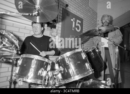 Apertura bunker pop Kleijwegt., Bunker, apertura, aperture, messa in uso, 24-02-1989 Whizgle News, Dutch Desk, Paesi Bassi, 1950-2000 Un musicista pratica su un set di batteria mentre un'altra persona si trova nelle vicinanze, tenendo un appunti e osservando lo spettacolo. L'ambiente suggerisce uno spazio di prova o uno studio, con una porta numerata visibile sullo sfondo. Foto Stock