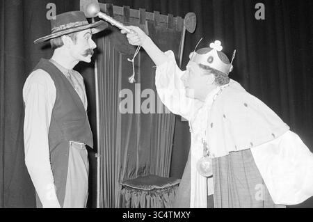 Spettacolo teatrale Whizgle News, Dutch Desk, The Netherlands, 1950-2000 Un interprete vestito da re, adornato con una corona e un abbigliamento regale, solleva drammaticamente uno scettro mentre si confronta con un altro personaggio, che indossa un cappello e baffi, suggerendo un momento teso o comico in una scena teatrale. Foto Stock