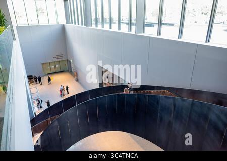 National Museum of African American History Stairway Washington DC // WASHINGTON DC - Una scala architettonica curva si snoda attraverso l'interno dello Smithsonian National Museum of African American History and Culture. Il museo, aperto nel 2016, è l'unico museo nazionale dedicato esclusivamente alla documentazione della vita, della storia e della cultura afroamericana. Progettato dall'architetto David Adjaye in collaborazione con il Freelon Group e Davis Brody Bond, l'edificio presenta una distintiva facciata a reticolo color bronzo ispirata all'arte yorubana e alle tradizioni del ferro americano. Il mus Foto Stock