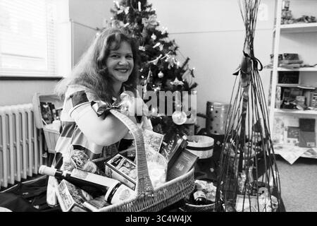 Anja Kramer, Christmas Packages, IJmuiden, IJmuiden, Paesi Bassi, 20-07-1997 Whizgle News, Dutch Desk, Paesi Bassi, 1950-2000 Una donna sorride mentre tiene un grande cestino pieno di varie bottiglie e dolcetti natalizi, circondato da un albero di Natale decorato e decorazioni natalizie. Foto Stock