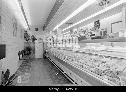 INTR. Butcher van 't Hoff en Zonen, Interior, 01-10-1974 Whizgle News, Dutch Desk, Paesi Bassi, 1950-2000 Una macelleria pulita e ordinata con una vetrina piena di varie carni confezionate. Le pareti sono piastrellate, adornate con alcune decorazioni, mentre scaffali e cestini mostrano prodotti aggiuntivi. L'illuminazione soffusa migliora l'atmosfera invitante, con un orologio visibile sulla parete. Foto Stock