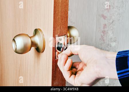 Durante il processo di installazione della bulloneria, l'operatore inserisce la vite nel foro da incasso della piastra di chiusura sulla nuova piastra di fissaggio della porta in legno. Foto Stock