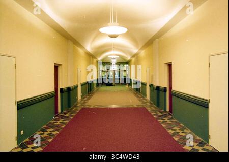 Sacred Heart Church, Apartments, Haarlem, Paesi Bassi, 02-09-1998 Whizgle News, Dutch Desk, Paesi Bassi, 1950-2000 Un lungo corridoio con soffitto curvo e luci dall'alto conduce verso un ingresso in vetro, fiancheggiato da porte su entrambi i lati. Il pavimento presenta una combinazione di piastrelle e moquette a motivi geometrici, che migliorano il senso di profondità e prospettiva nello spazio. Foto Stock