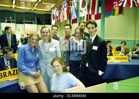 United Nations Students Conference, Haarlem, Paesi Bassi, 24-04-1998 Whizgle News, Dutch Desk, paesi Bassi, 1950-2000 Un gruppo di giovani individui posa insieme in un ambiente formale, mostrando un mix di abbigliamento professionale. Si trovano di fronte a un lungo tavolo adornato con cartelli che rappresentano vari paesi, mentre bandiere da tutto il mondo sono appese sopra la testa, creando un'atmosfera internazionale. Foto Stock
