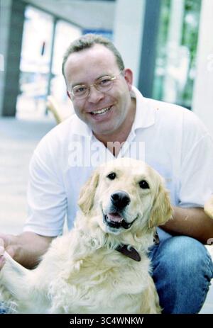 Ritratto dell'uomo con cane Whizgle News, Dutch Desk, Paesi Bassi, 1950-2000 Un uomo sorridente siede comodamente mentre interagisce giocosamente con un allegro Golden retriever, entrambi godendosi un momento di compagnia. Foto Stock