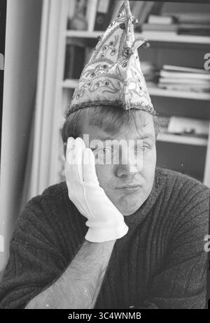 Ritratto di un uomo con un cappello di carnevale, 00-02-1995 Whizgle News, Dutch Desk, Paesi Bassi, 1950-2000 Una persona che indossa un cappello decorativo da festa poggia il mento su una mano, mostrando un'espressione premurosa o non impressionata, mentre si veste casualmente con un maglione. Foto Stock