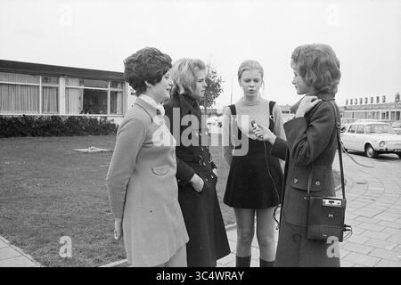 Report on working Youth, Report, 27-10-1970 Whizgle News, Dutch Desk, Paesi Bassi, 1950-2000 quattro donne stanno all'aperto, impegnate in conversazione. Una donna sta parlando in un microfono, mentre le altre ascoltano con attenzione. Sono vestiti con abiti eleganti tipici dell'epoca, sfoggiando un mix di raffinatezza e moda giovanile. Sullo sfondo, un edificio moderno e le auto parcheggiate aggiungono un contesto alla scena. Foto Stock