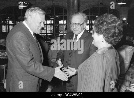 Ricevimento d'addio Mr. Blokker, HD, Haarlems Dagblad, ecc. e IJmuider Courant e Koeri, 14-02-1986 Whizgle News, Dutch Desk, Paesi Bassi, 1950-2000 Un incontro formale con tre persone in conversazione, dove due uomini, vestiti in abiti, sono impegnati in una stretta di mano, mentre una donna con un abito elegante osserva e sorride. L'ambiente sembra essere una vivace atmosfera sociale con luci soffuse sullo sfondo. Foto Stock