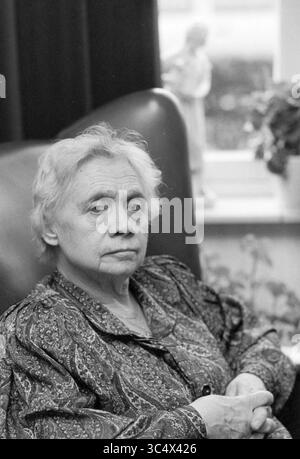 Sig.ra Van Dijk per quanto riguarda casa bruciata, incendi, vigili del fuoco, 13-04-1989 Whizgle News, Dutch Desk, i Paesi Bassi, 1950-2000 una donna anziana con un'espressione seria siede con cura in una posa rilassata, con le mani appoggiate in grembo. Indossa una camicetta a motivi geometrici ed è circondata da un ambiente accogliente che suggerisce una vista dalla finestra e una figura decorativa sullo sfondo. Foto Stock