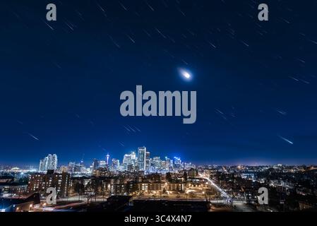 20 aprile 2018 - Alberta, Canada - un percorso urbano stellare! È possibile! Si tratta di una pila di 275 esposizioni di 2 secondi per creare le piste stellari di Orion, la Luna e le stelle dell'inverno sul centro di Calgary il 19 aprile 2018. Il cielo era nebbioso, e naturalmente c'era l'inquinamento luminoso della città e la luce della luna, ma la telecamera ha comunque rilevato un buon numero di stelle. ..le 275 esposizioni forniscono cielo e terra. Un'immagine finale, scattata 1 minuto dopo l'ultima immagine della traccia stellare e unita alla modalità Schiarisci, aggiunge le stelle a punta alla fine, per definire meglio le costellazioni e la m. Foto Stock
