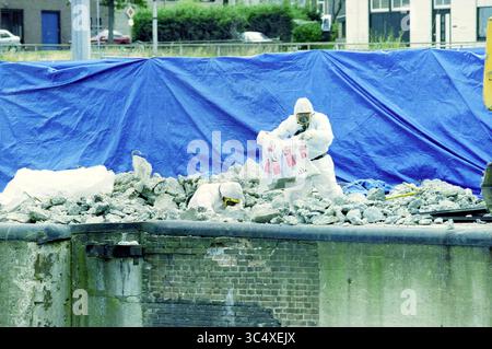 Amianto a Zuidersluis, IJmuiden, IJmuiden, Nederland, 26-07-1999 Whizgle News, Dutch Desk, Paesi Bassi, 1950-2000 due persone che indossano tute protettive si trovano in un cantiere, maneggiando detriti e macerie mentre lavorano in un'area coperta da un telone blu. Le loro azioni attente suggeriscono che sono impegnati in un processo di pulizia o demolizione di materiali pericolosi. Foto Stock