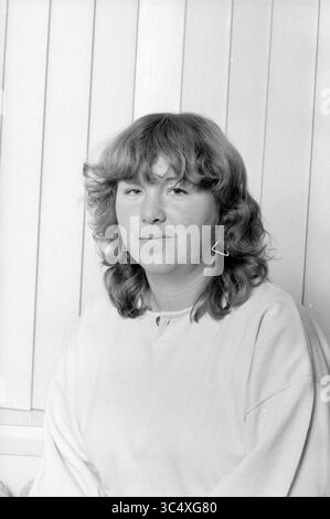 Ritratto donna, 00-00-1984 Whizgle News, Dutch Desk, Paesi Bassi, 1950-2000 Una giovane donna con capelli ricci e orecchini distintivi siede tranquillamente, guardando direttamente lo spettatore. La sua espressione è calma e premurosa, sullo sfondo di linee verticali che creano un senso di profondità. Foto Stock