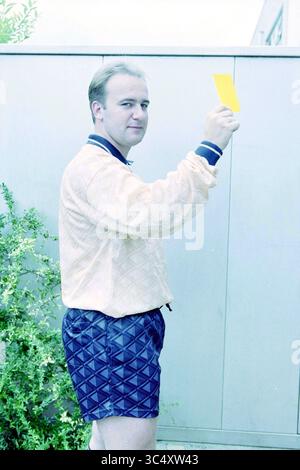 Ben van Looy, arbitro, Velserbroek, 09-08-1999 Whizgle News, Dutch Desk, i Paesi Bassi, 1950-2000 Un uomo con una giacca di colore chiaro regge un cartellino giallo, in piedi con un leggero sorriso, circondato dal verde. Indossa pantaloncini a motivi geometrici, aggiungendo un tocco giocoso al suo outfit. Foto Stock
