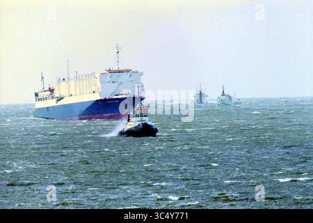 Barca tra i moli, IJmuiden, IJmuiden, Paesi Bassi, 27-10-1998 Whizgle News, Dutch Desk, Paesi Bassi, 1950-2000 Un rimorchiatore naviga attraverso le acque instabili, assistendo una grande nave da carico che attraversa il porto, con un'altra nave visibile sullo sfondo. La scena cattura il movimento dinamico delle operazioni marittime contro un ampio mare aperto. Foto Stock