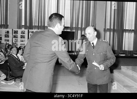 COM. Installazione Miller, polizia, 02-05-1980 Whizgle News, Dutch Desk, Paesi Bassi, 1950-2000 due individui sono impegnati in una stretta di mano durante un evento formale. Una persona, vestita in abbigliamento militare, sembra presentare qualcosa, possibilmente un certificato o un premio, all'altra, che è anche in abbigliamento formale. Sullo sfondo, un pubblico è seduto, osservando l'interazione, con esposizioni visive o fotografie disposte sulle pareti. L'ambientazione suggerisce una cerimonia o un evento di riconoscimento. Foto Stock