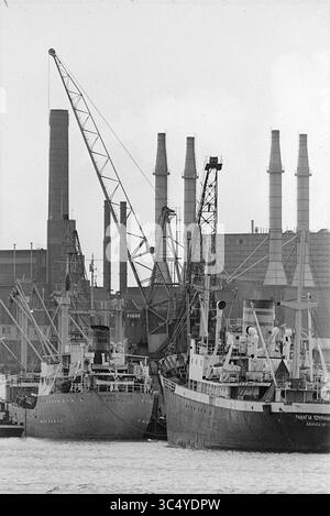 Port, IJmuiden, Paesi Bassi, 00-11-1969 Whizgle News, Dutch Desk, i Paesi Bassi, 1950-2000, Un vivace panorama industriale sul lungomare, caratterizzato da grandi navi da carico attraccate fianco a fianco, con torreggianti gru e ciminiere sullo sfondo, che evidenziano l'attività del commercio marittimo e della movimentazione merci. Foto Stock