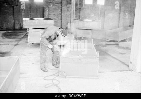 Costruzione di magazzino frigorifero, Kwakelstein [W. Kwakkelstein BV], costruzione, pozzi di costruzione, 06-06-1972 Whizgle News, Dutch Desk, nei Paesi Bassi, 1950-2000 Un lavoratore in indumenti protettivi utilizza una torcia di saldatura per riparare un contenitore metallico in un ambiente industriale spazioso, circondato da contenitori vuoti e pareti in mattoni. L'aria viene riempita con scintille e fumo proveniente dal processo di saldatura. Foto Stock