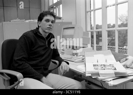 Dipendenti del museo Frans Hals, Haarlem, Nederland, 24-11-1999 Whizgle News, Dutch Desk, i Paesi Bassi, 1950-2000 anni Un giovane uomo siede su una scrivania disordinata, circondato da documenti e computer, guardando attentamente verso lo spettatore. La luce del sole scorre attraverso grandi finestre, illuminando l'area di lavoro piena di accenni di creatività e concentrazione. Foto Stock