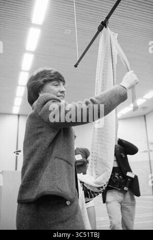 Apertura della sala eventi Noordwijkerhout da parte della Principessa Margriet, ricevimenti reali e visite reali, apertura, apertura, messa in servizio, Noordwijkerhout, 22-01-1982 Whizgle News, Dutch Desk, Paesi Bassi, 1950-2000 Una donna con un cappotto su misura sorride mentre regge un grande pezzo di tessuto, mostrandolo con entusiasmo. In background, le persone con telecamere osservano la dimostrazione, suggerendo un evento significativo o una mostra relativa al tessile o al design. Foto Stock