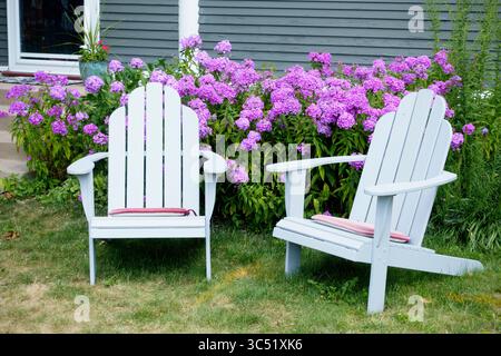 Un paio di classiche sedie Adirondack, originarie delle montagne Adirondack nella parte settentrionale dello stato di New York, di fronte ai fiori viola phlox. St Paul, Minnesota, Minnesota, Stati Uniti Foto Stock