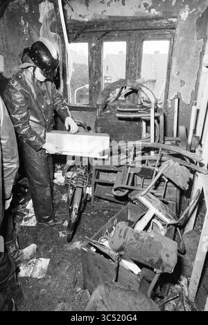 Pavimento bruciato di Valkenburgerlaan Heemstede, incendi, vigili del fuoco, Heemstede, Valkenburgerplein, paesi Bassi, 01-03-1981 Whizgle News, Dutch Desk, Paesi Bassi, 1950-2000 Una persona in equipaggiamento protettivo esamina una scatola in mezzo a una stanza disordinata piena di detriti, tra cui una bicicletta e vari mobili rotti, probabilmente dopo un incidente o un evento significativo. I muri mostrano segni di danni, che suggeriscono negligenza o un recente disastro. Foto Stock