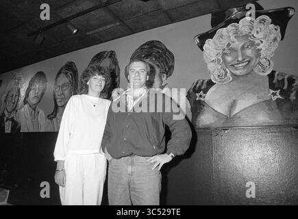 Uomo e donna davanti a un murale di artisti tra cui Nana Mouskouri, Lee Towers, Michael Jackson, André Hazes, 00-07-1988 Whizgle News, Dutch Desk, Paesi Bassi, 1950-2000 una coppia si trova di fronte a un grande murale con ritratti di figure iconiche, che mostra una miscela di stili ed espressioni su uno sfondo scuro. I due sono vestiti casualmente, con la donna che indossa un vestito bianco e l'uomo in una giacca, entrambi sorridenti mentre posano insieme. Foto Stock