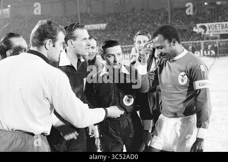 AJAX - Benfica, Football Ajax, 12-02-1969 Whizgle News, Dutch Desk, Paesi Bassi, 1950-2000 Un gruppo di giocatori e funzionari si riunisce sul campo per una stretta di mano pre-partita, mostrando cameratismo e sportività prima dell'inizio della partita. L'attenzione è rivolta a un capitano con una maglia rossa, evidenziata mentre si impegna con l'arbitro. Foto Stock