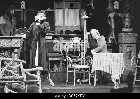 Cabaret Brakke Grond, Cabaret, Amsterdam, Nes, Paesi Bassi, 10-09-1975','11-09-1975 Whizgle News, Dutch Desk, Paesi Bassi, 1950-2000 Una scena drammatica si svolge sul palco, con una donna in un cappotto elegante, trasudando fiducia mentre si rivolge al pubblico. Nelle vicinanze, un uomo siede inseguito su un tavolo, la sua espressione di stanchezza o contemplazione. Lo sfondo include una serie di mobili d'epoca ed elementi teatrali, suggerendo un'intrigante narrazione tra i personaggi. Foto Stock