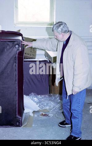 Sig. Wotte, Hillegom, 09-03-1999 Whizgle News, Dutch Desk, Paesi Bassi, 1950-2000 Un uomo con una giacca beige esamina un mobile di colore scuro, in piedi tra scatole e materiali di imballaggio sparsi in una stanza che sembra essere nel mezzo di un'organizzazione o di un trasloco. Foto Stock